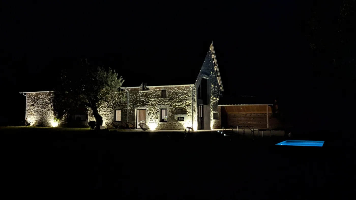 La grange en pierre du Gîte du Longeard éclairée de nuit, la piscine illuminée en contrebas